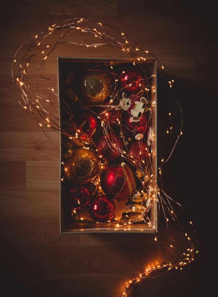 A cozy flat lay of Christmas ornaments in a box adorned with string lights.